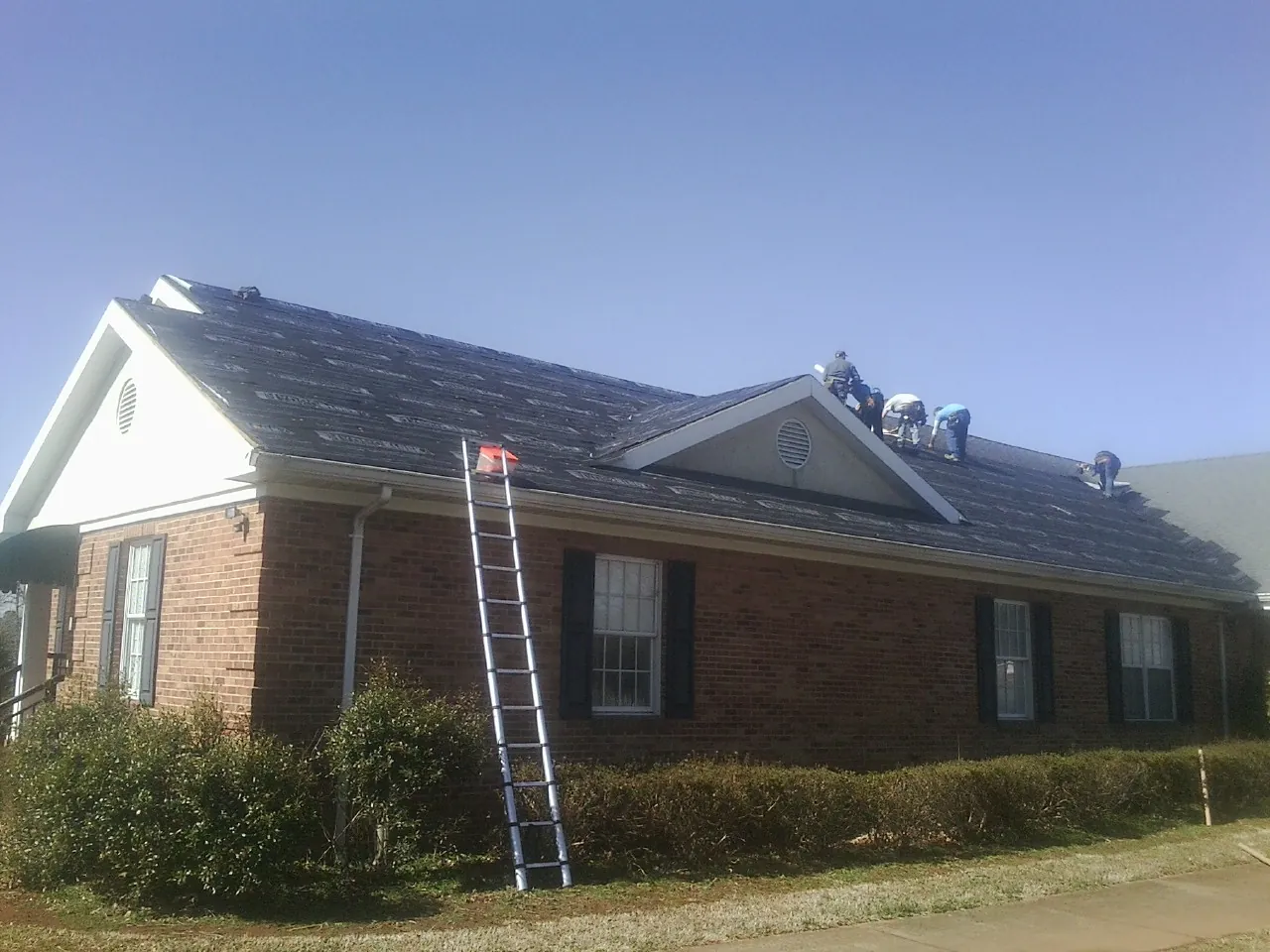 Crew tearing shingles off a brick ranch roof with a ladder set — Emergency Roof Repair work by our crew in Keasbey