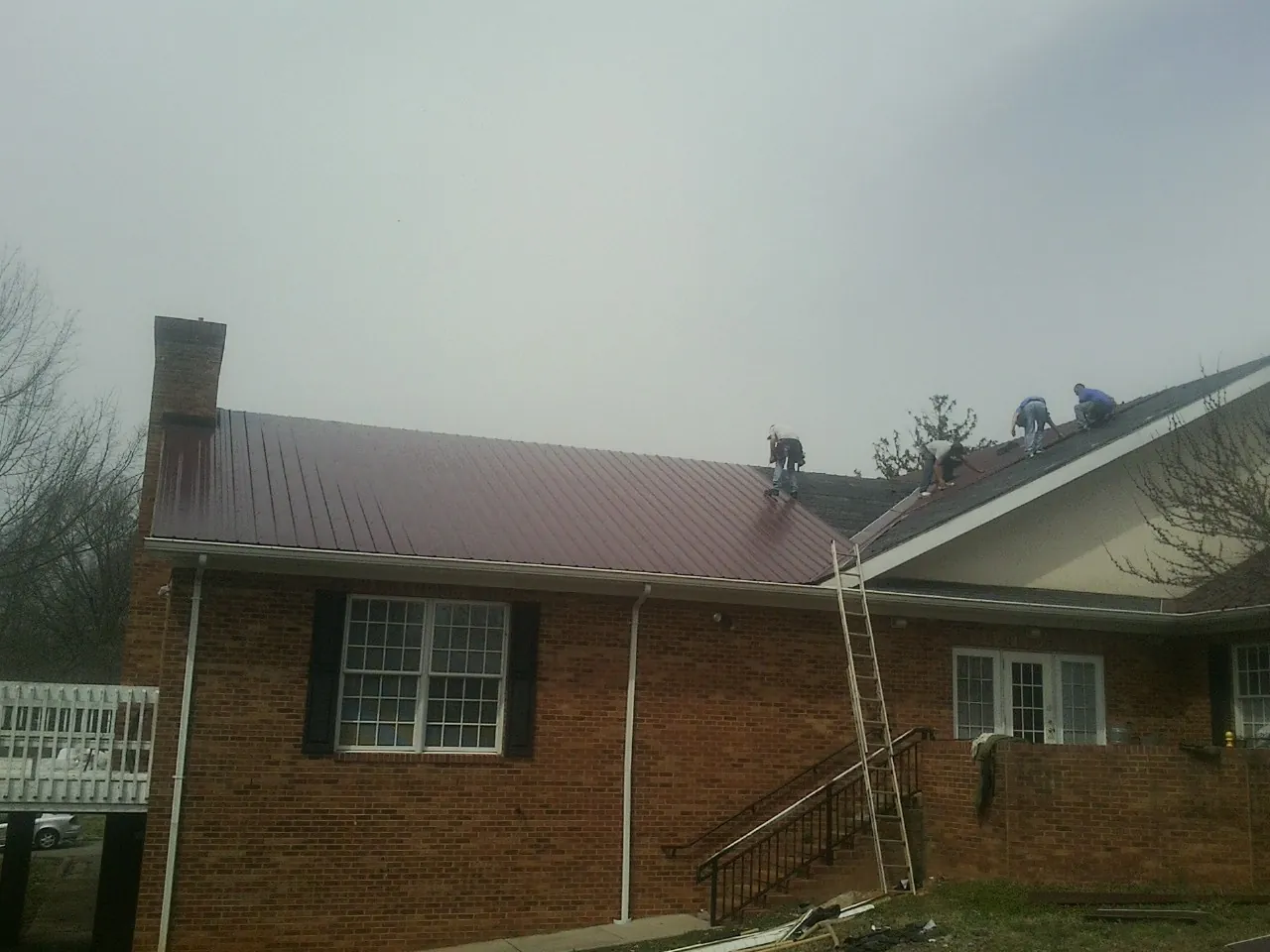 Crew setting red metal roofing panels on a brick home in Keasbey
