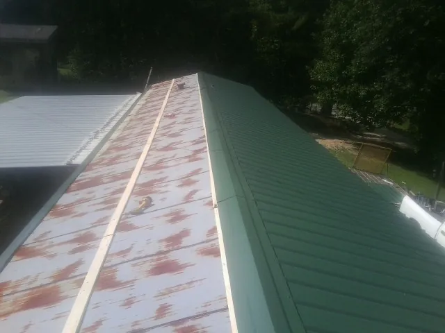 Old rusted panels beside newly installed green metal roofing — Wind Damage Roof Repair by Roofing Brothers in Keasbey