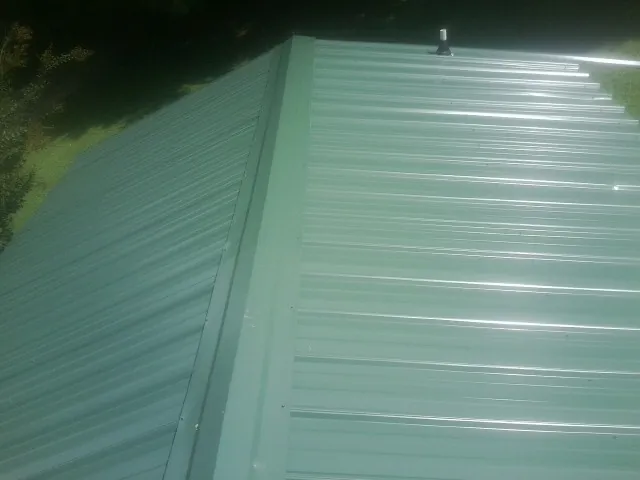 New green metal panels meeting at the ridge of a roof — Flat Roof Repair work by our crew in Keasbey