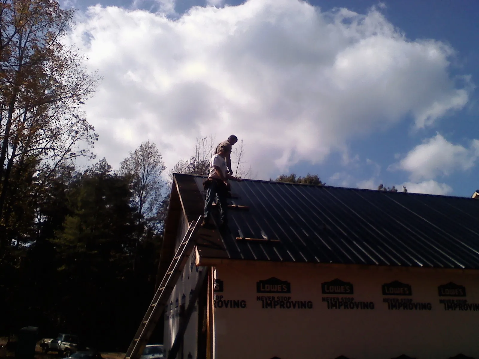Roofer fastening dark metal panels high against a cloudy sky, from a Roof Inspection job in Keasbey
