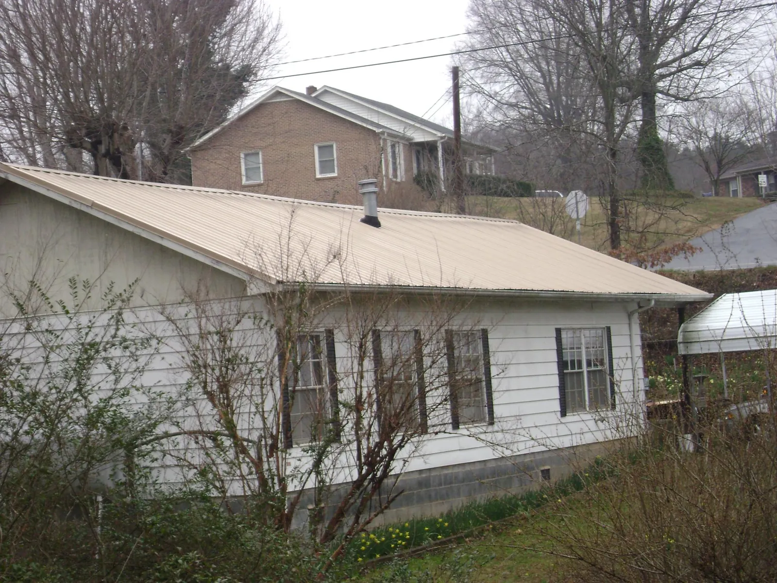 Tan metal roof on a white sided house set into a hillside — Commercial Roofing by Roofing Brothers in Keasbey